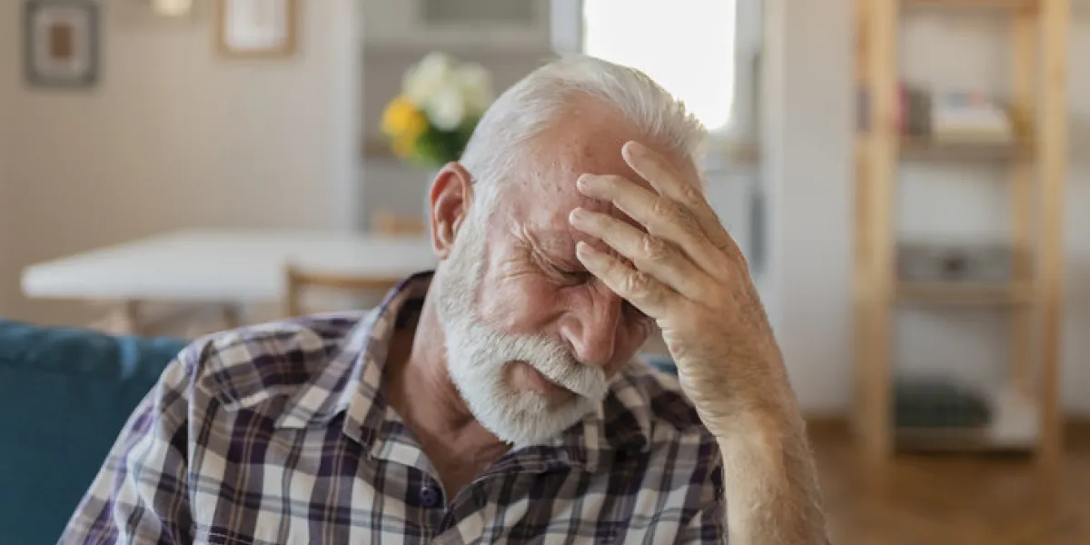 shot of a senior man with a headache holding his head while sitting on a sofa at home in the living room shot of an uncomfortable looking elderly man holding his head in discomfort due to pain at home during the day
