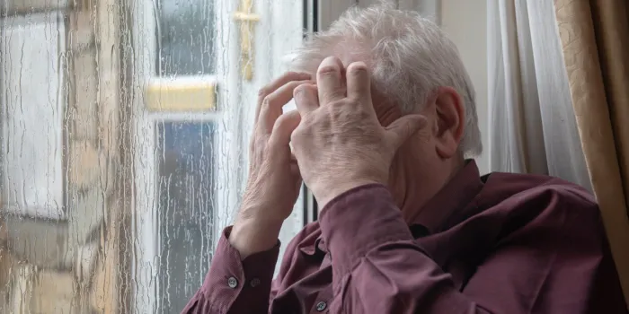 stressed senior man with head in hands on a rainy day