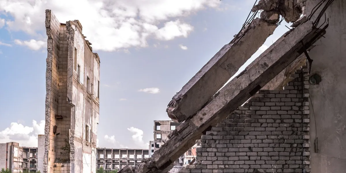 a ruined brick wall with load-bearing beams against the background of the remains of a large building and a sky with clouds background