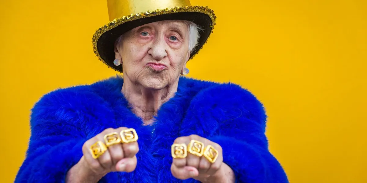 funny and extravagant senior woman posing on colored background - youthful old woman in the sixties having fun and partying