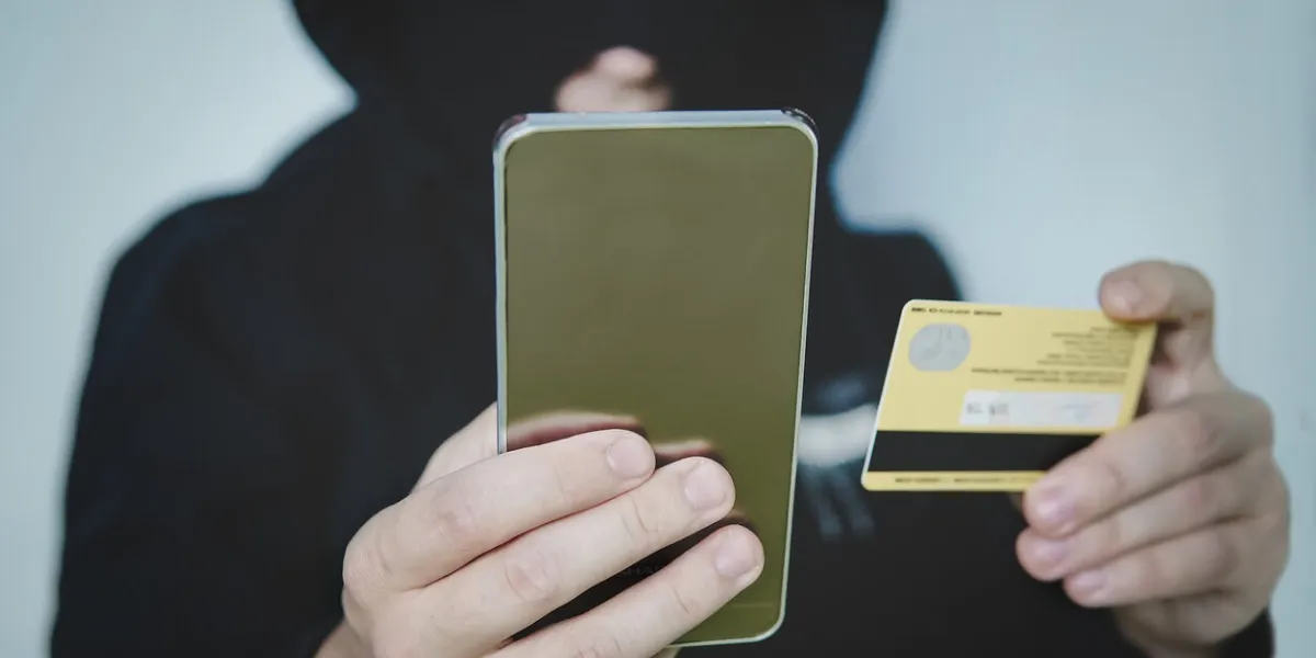 cyber criminal in balaclava enters the information of a personal bank account credit card fraudulent scheme stealing cyber money using mobile new ways of fraudulent transactions via online banking