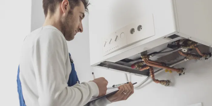 professional plumber servicing a boiler and writing on a clipboard