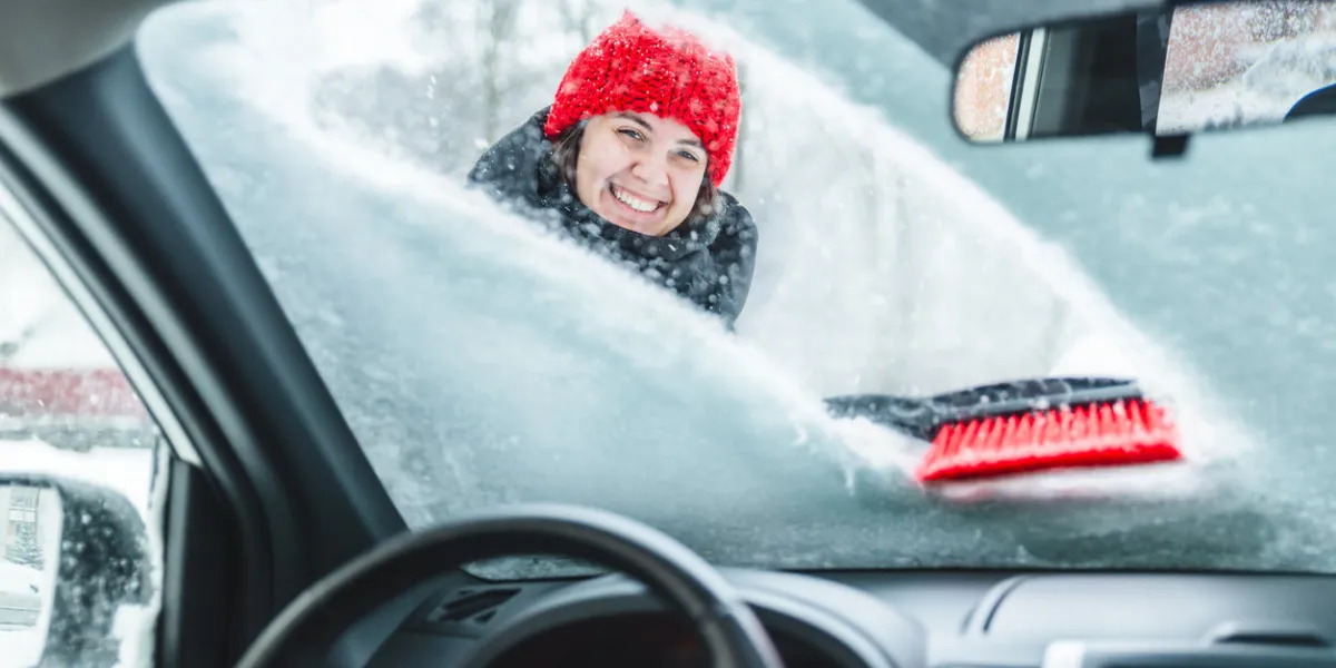 young pretty woman cleaning car after snow storm blizzard