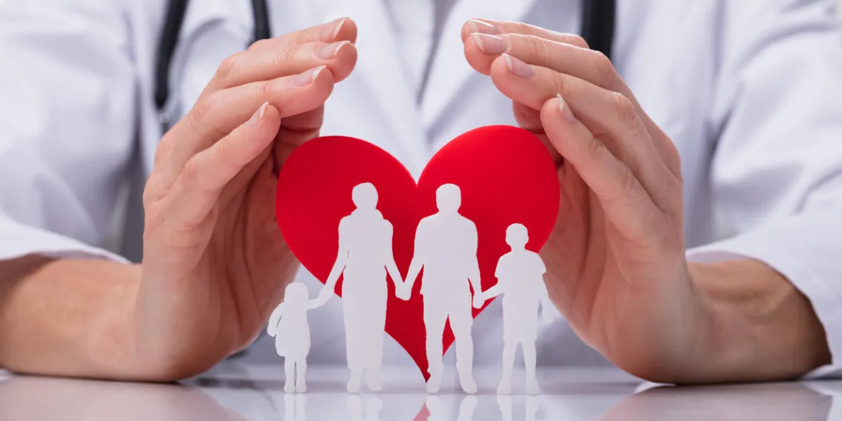 close-up of a doctor's hand protecting family cut out with red heart shape