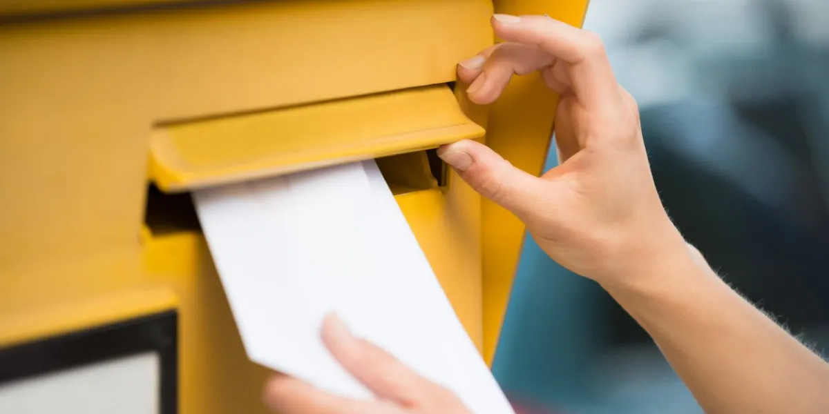 closeup of woman's hands inserting letter in mailbox