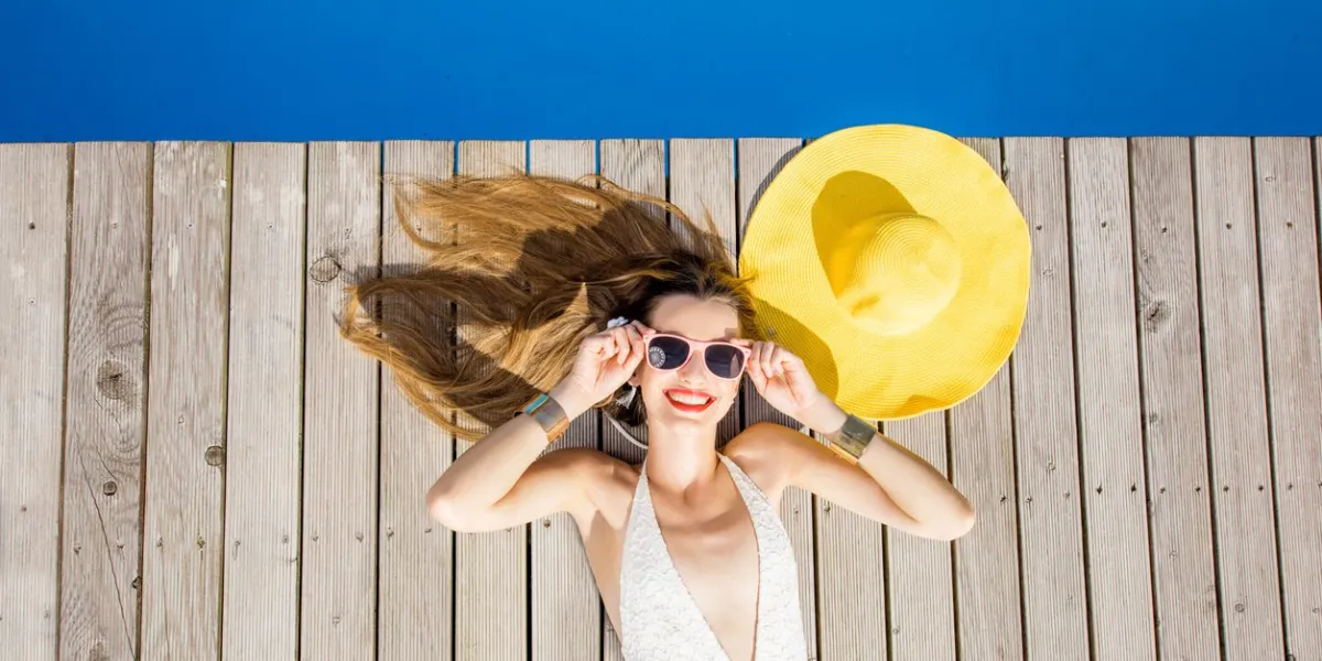 playful woman lying with yellow sunhat on the poolside summer vacation concept