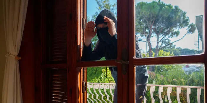 thief in balaclava peeks through the windows