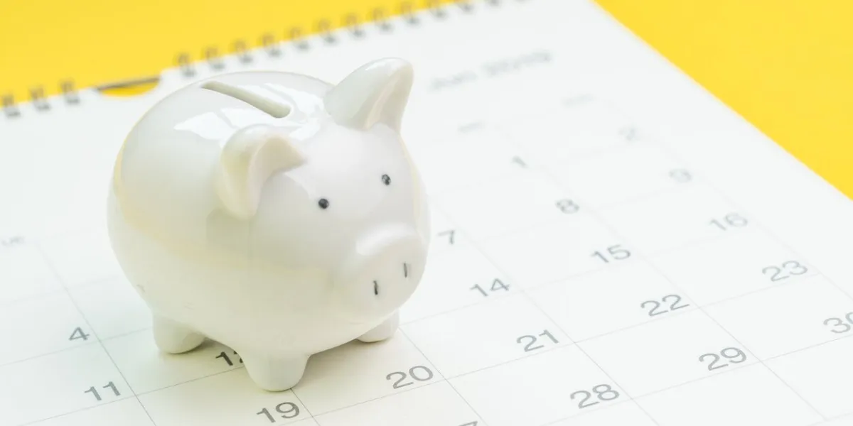finance, saving money or salary pay day, white piggy bank on white clean calendar on solid yellow background