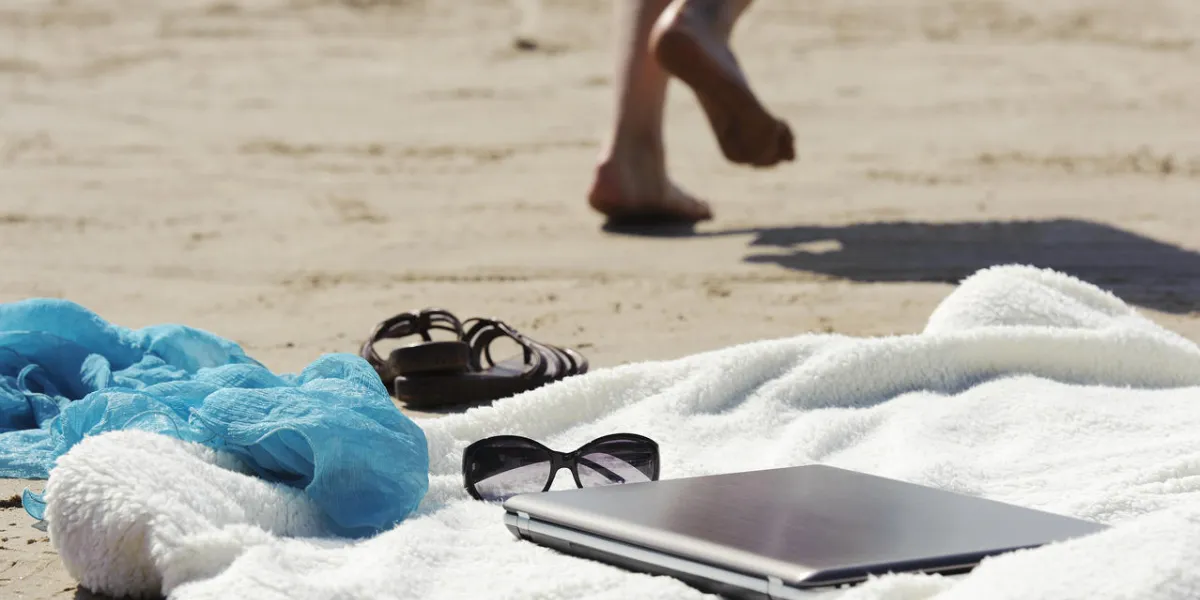 wrap, ordinateur portable, écharpe, lunettes de soleil et mules allongé sur la plage en été femme jambes