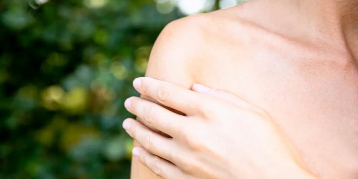 female hand on painful bare shoulder outdoors in green nature woman with hand on bare shoulder, close-up copy space