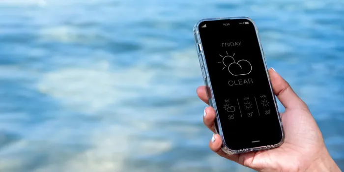 weather forecast on smartphone clear weather, display app on friday with temperature number, cloud and sun icons on mobile smart phone screen in hand on blue sea water background with copy space