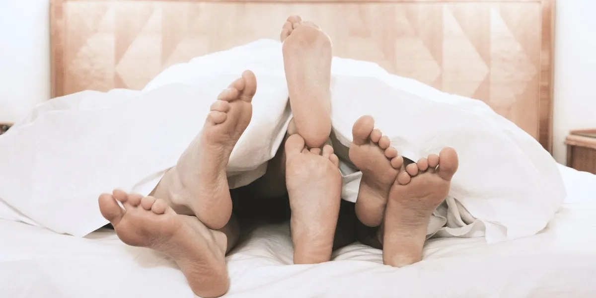 three pairs of feet lying together under bed cover in bedroom, t