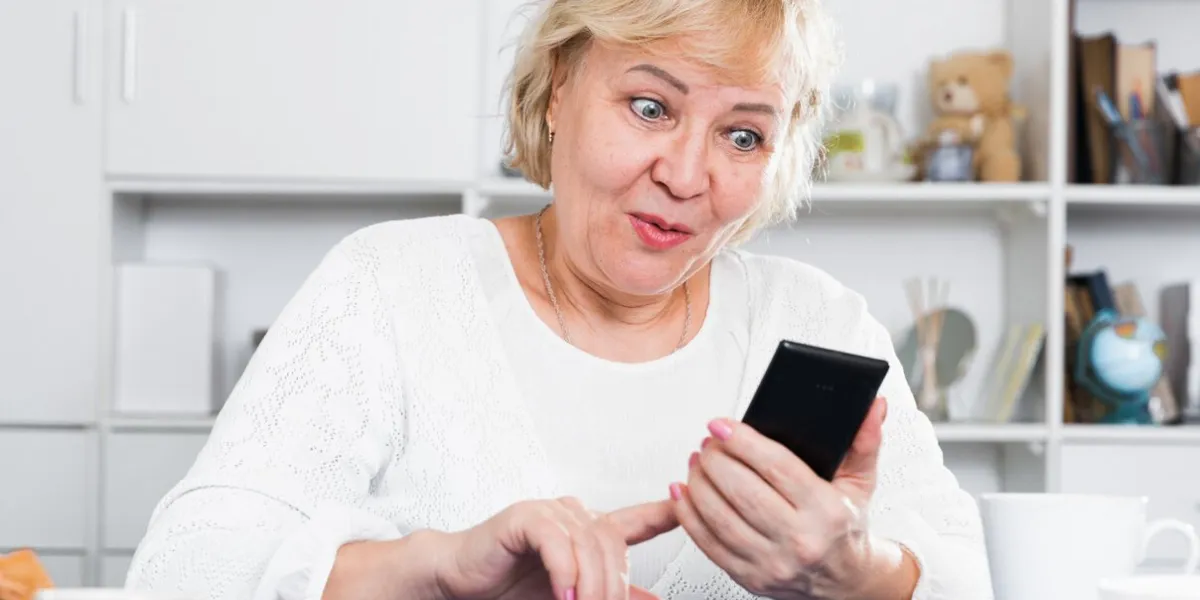 mature woman enjoys a modern smartphone while sitting at home at a table