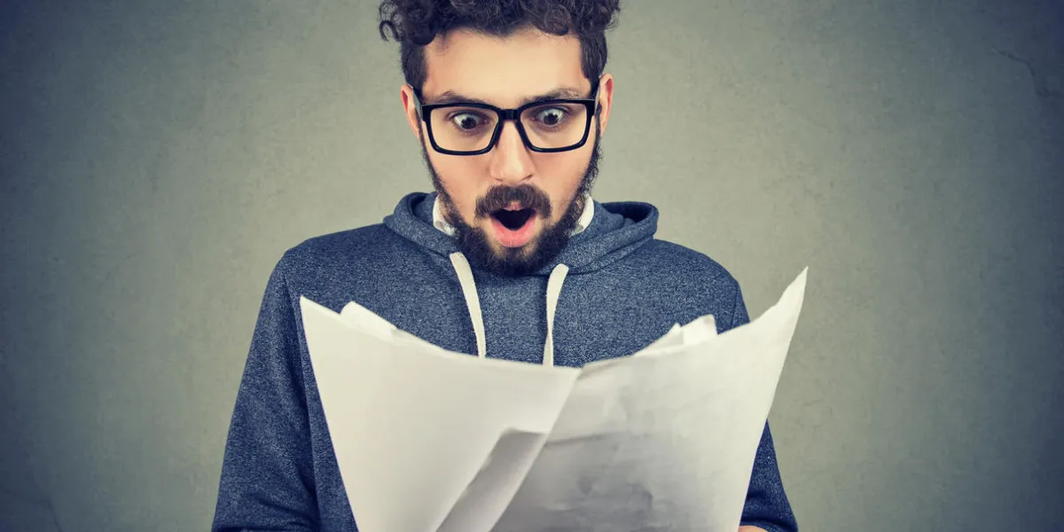 handsome man in eyeglasses exploring documents and looking shocked with results