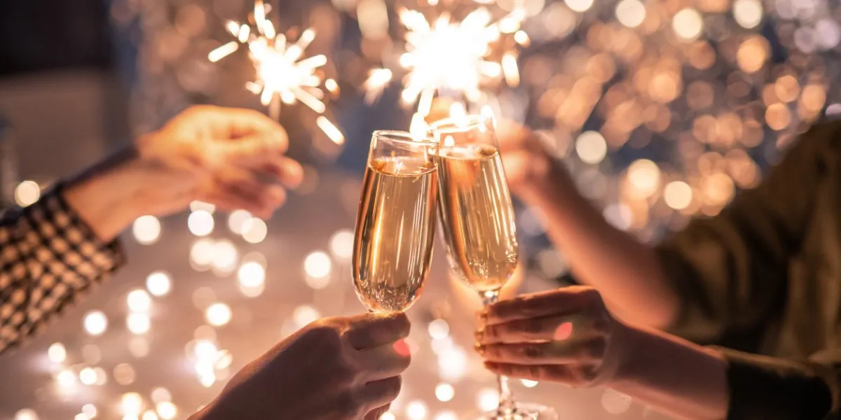 hands of couple clinking with flutes of champagne and their friends holding sparkling bengal lights