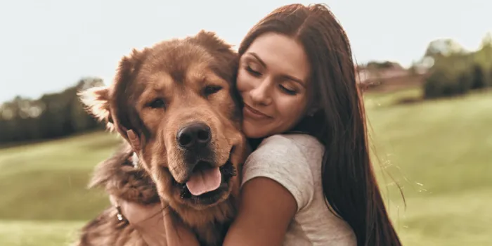 beautiful young woman keeping eyes closed and smiling while embracing her dog outdoors