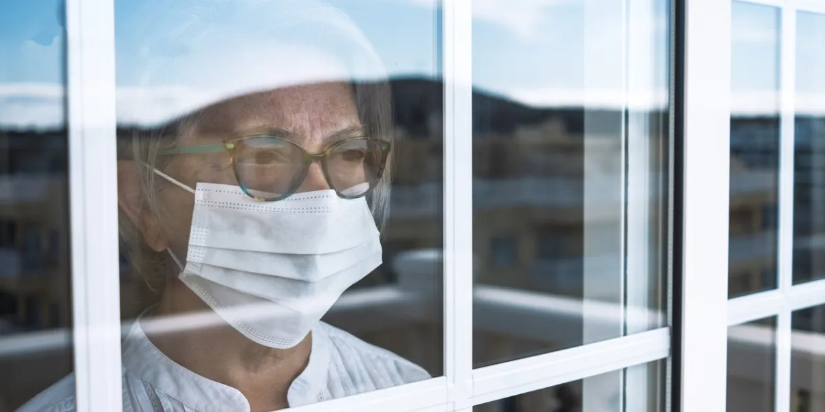 coronavirus pandemic, senior woman in self quarantine to avoid contagion of infection by virus covid-19 stays home looking outdoor from the window prevention concept