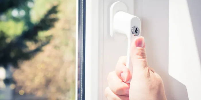 a male hand holding a lockable window handle of a closed white window with trees in background, prevent burglary concept