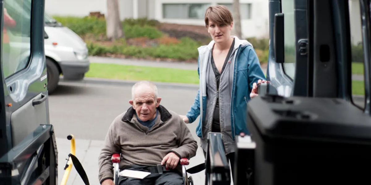man in wheelchair entering a modified van shot from inside the vehicle, and with a female support worker by his side