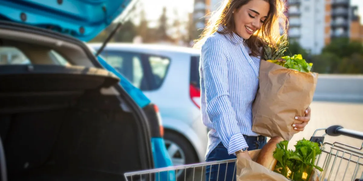 caucasian brunette going holding paper bags with food products young woman putting package with groceries and vegetables into car trunk attractive caucasian female shopping in mall or grocery store