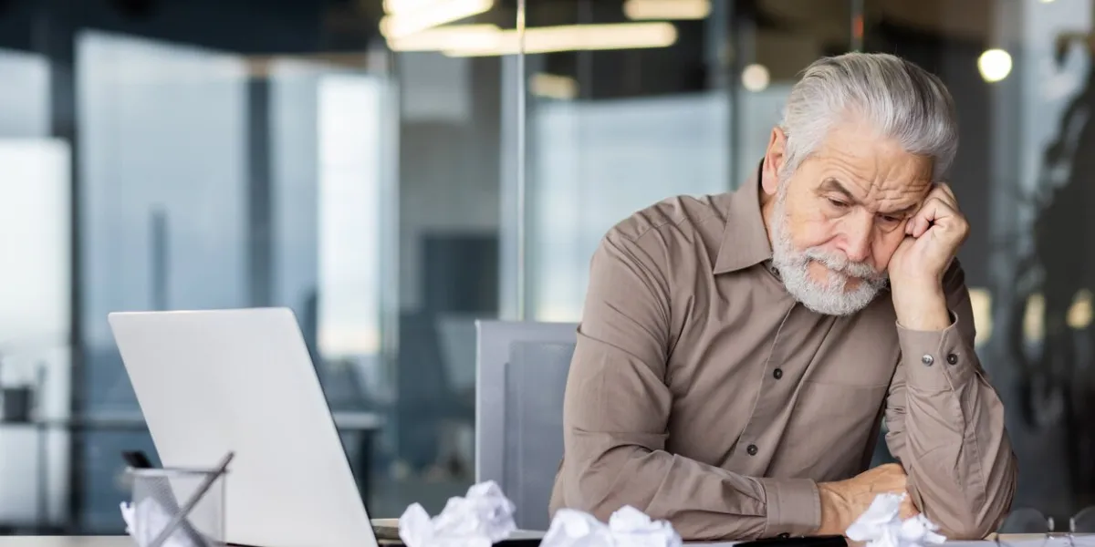 upset frustrated gray haired boss sitting inside office at workplace, mature man old businessman in shirt working with laptop, unhappy with company achievement results and negative reports