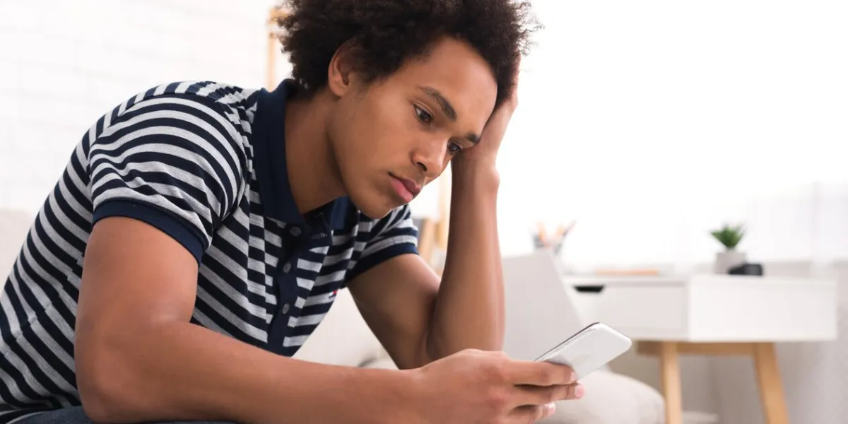horrible day depressed teenage boy looking at his smartphone screen while sitting on sofa at home, copy space