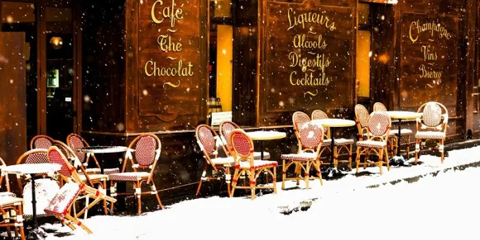 wooden parisian coffee house with it's sidewalk tables and chairs in winter with the snow falling