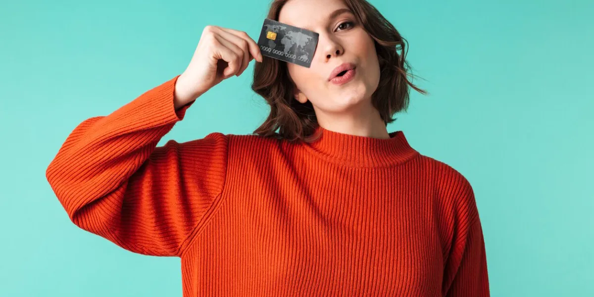 portrait of a pretty young woman dressed in sweater holding credit card at her face isolated over blue background
