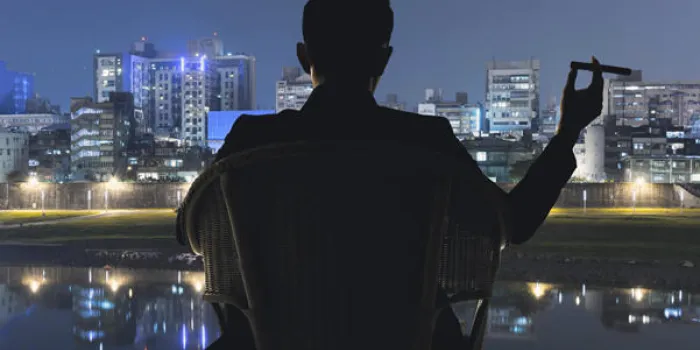 silhouette d'homme d'affaires s'asseoir sur une chaise et tenir un cigare et en regardant la ville dans la nuit