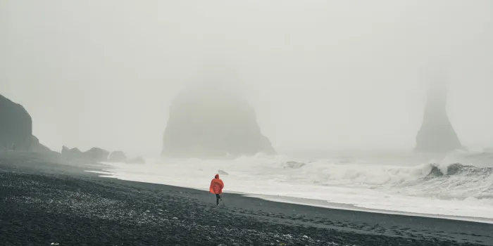 famous black sand beach vik in iceland person in red raincoat running by the sea shore in the fog