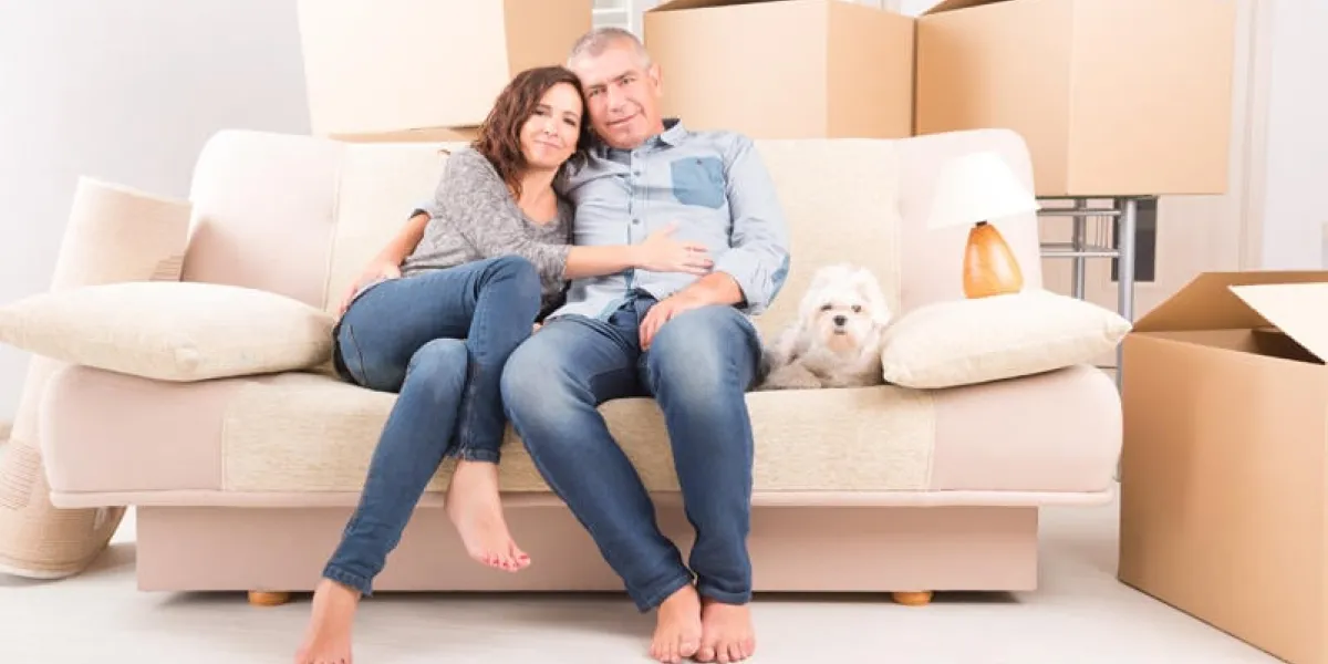 happy mature couple celebrating their new home sitting together on the sofa with their little dog just after moving in