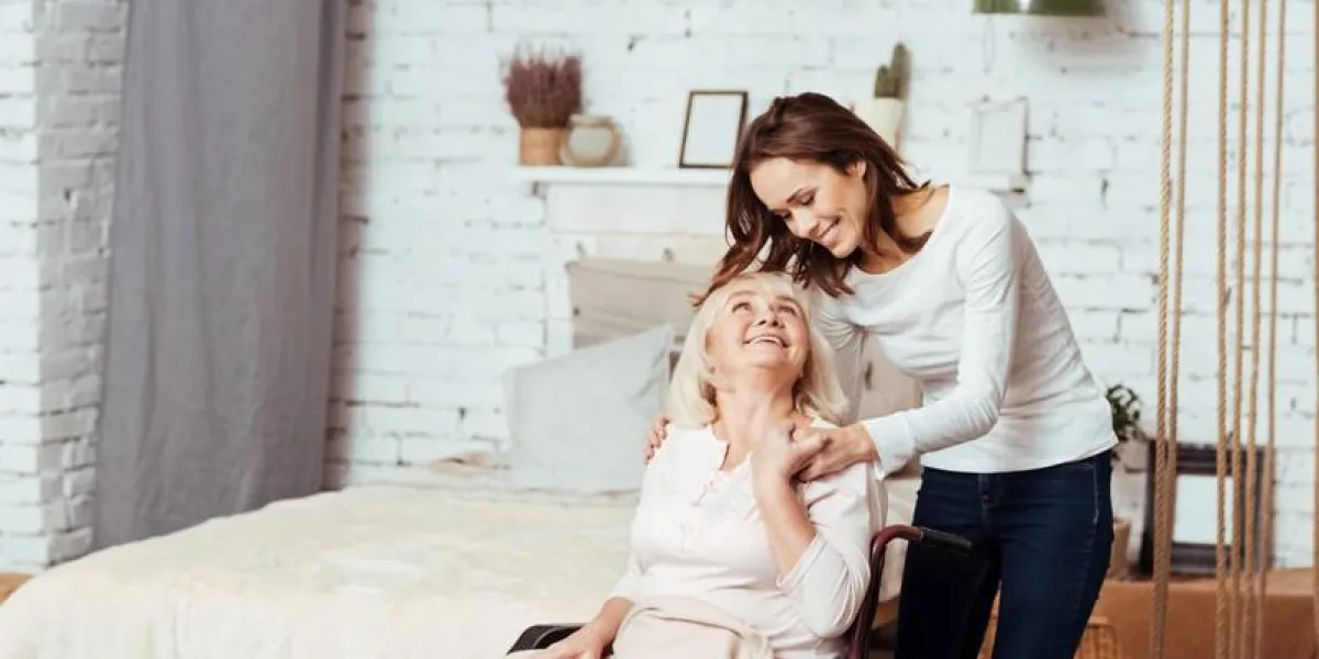 nice carer joyful delighted old woman sitting in wheelchair and lookign at her granddaughter who is takign care of her