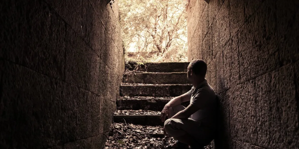 young man sits inside of dark stone tunnel with glowing end, warm tonal correction photo filter