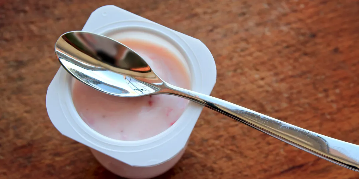 strawberry pink yogurt in white plastic cup on a wooden rustic background with spoon on it