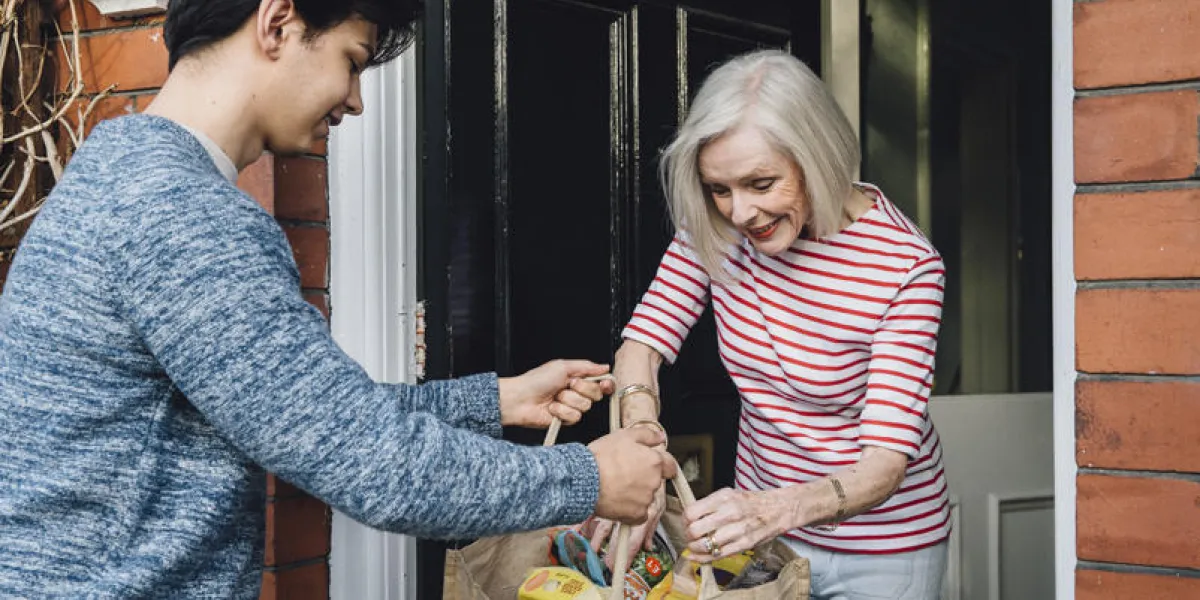 teenage boy is delivering some groceries to an elderly woman he is handing her a shopping bag at her front door