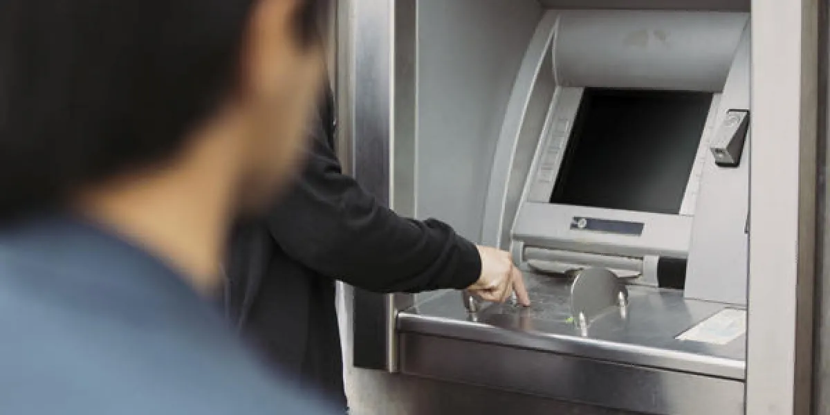 homme retirant de l'argent à un guichet automatique avec un voleur qui le suit