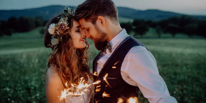 beautiful young bride and groom on a meadow in the evening, holding sparklers