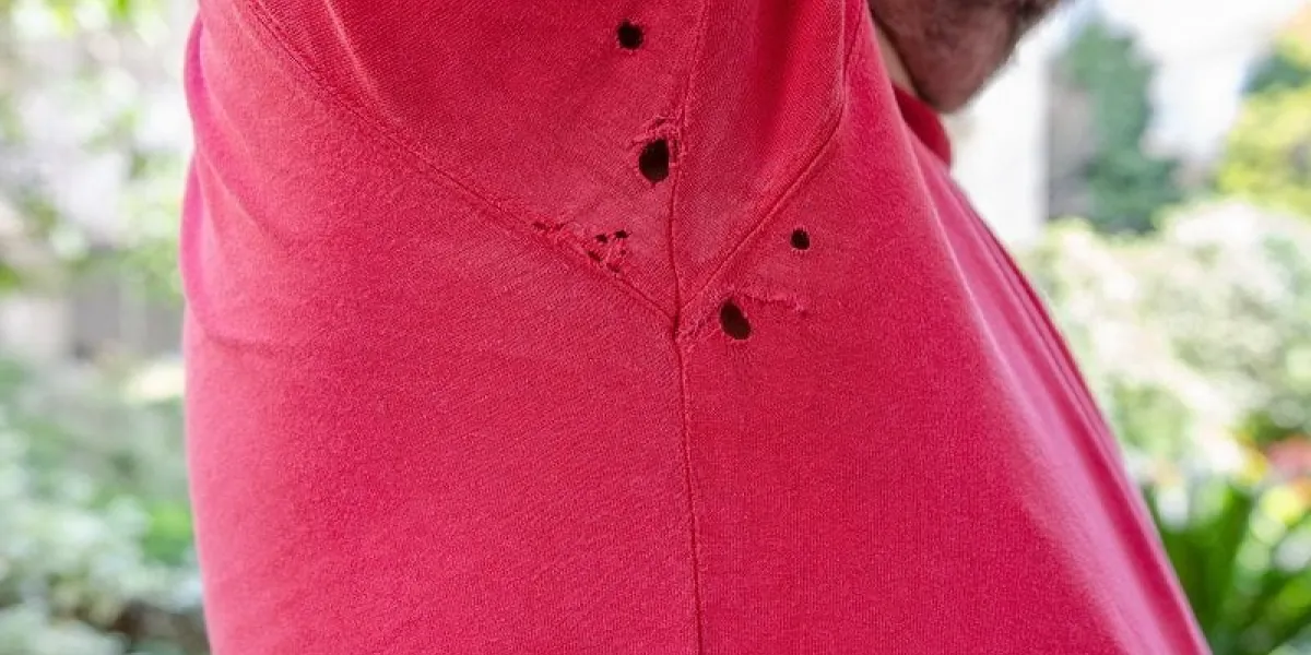 the holes in a t-shirt shot close up the face of the man is not visible a piece of beard and a street background out of focus