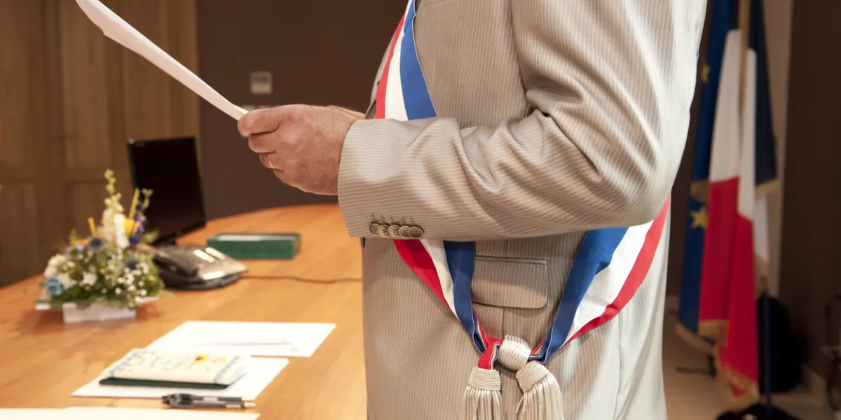 a french mayor reads a paper in a wedding room he wears the scarf of the mayor close-up