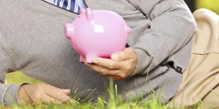 souriant matures gentleman allongé sur une herbe verte et tenant une tirelire dans un parc