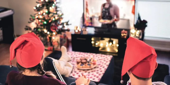 couple watching tv on christmas happy family holiday at home man and woman on couch relaxing with tree, decorations, lights, candles and television modern city celebrations merry xmas