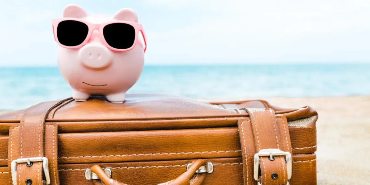 pink piggy bank in sunglasses on leather travel case over sea beach background savings for vacation concept