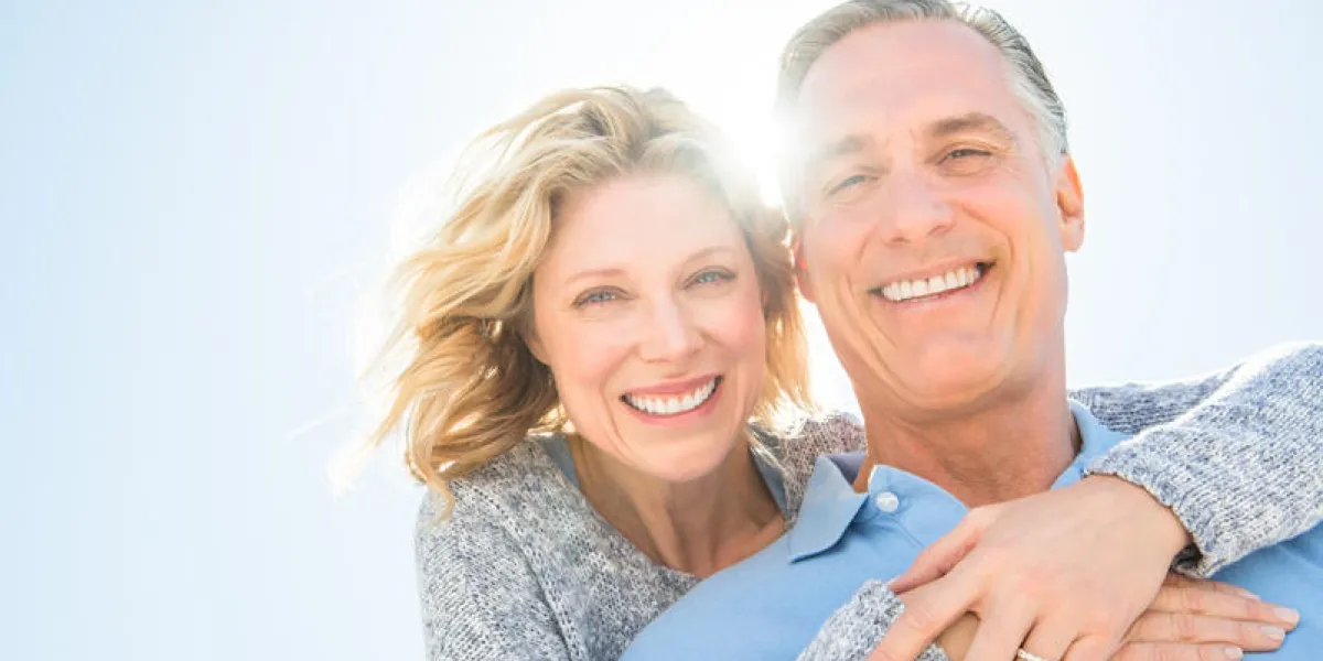 low angle portrait of cheerful mature woman embracing man from behind against clear sky