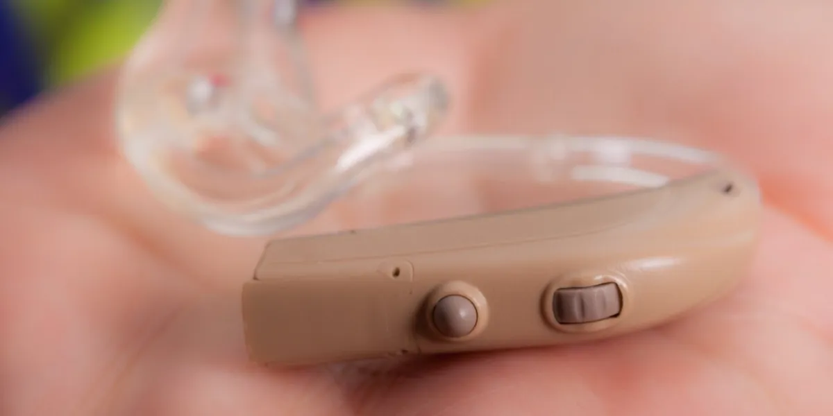 closeup senior woman with electronic hearing aid in her hand health care, hear disorder, device for the deaf