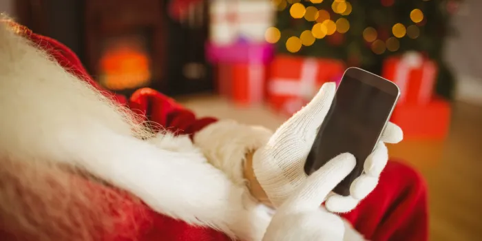 santa claus touching a smartphone at christmas at home in the living room