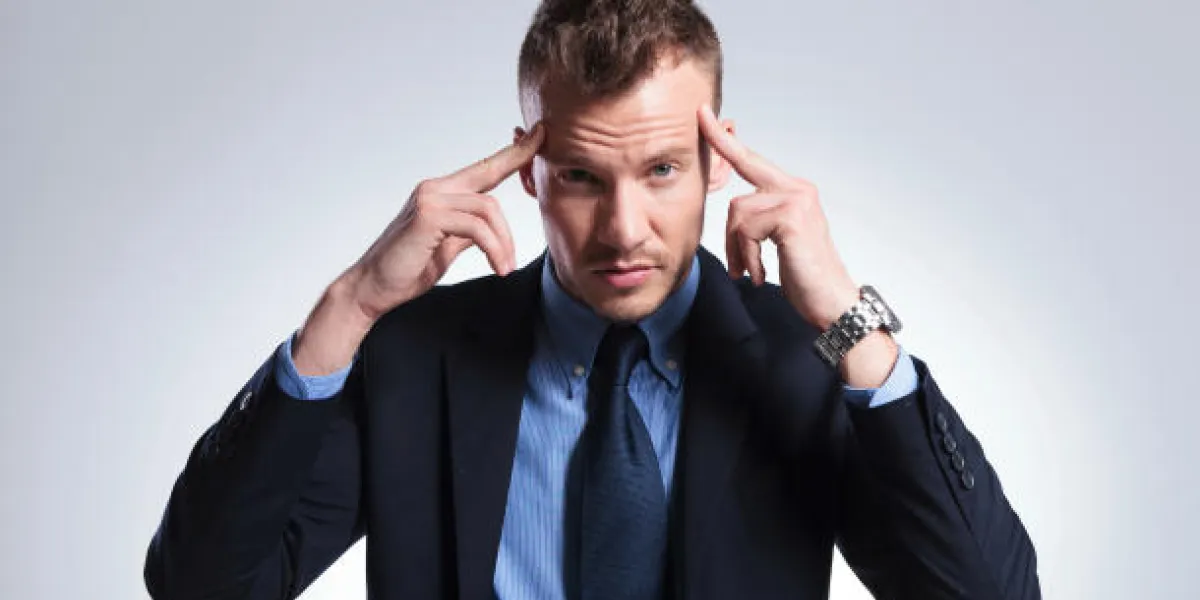 homme d'affaires jeune se concentrant avec ses doigts sur ses tempes tout en regardant dans la caméra sur un fond de studio gris clair