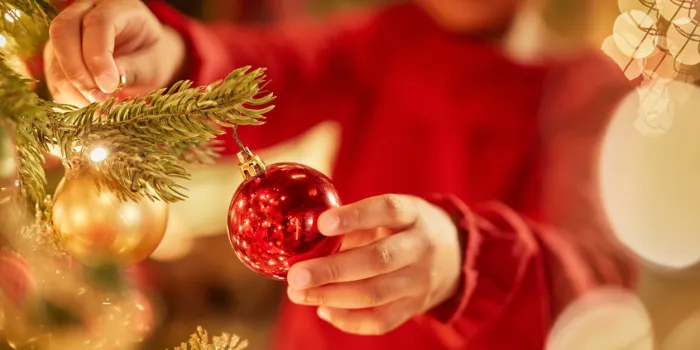 closeup of unrecognizable little girl decorating christmas tree with ornaments and twinkling lights, copy space