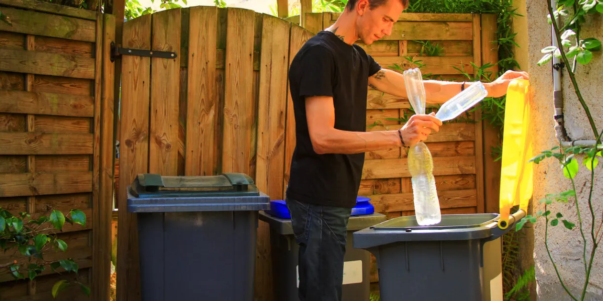 man putting plastic bottles in a yellow bin for recycling