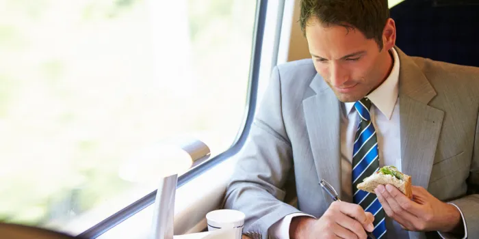 businessman eating sandwich on train journey and working