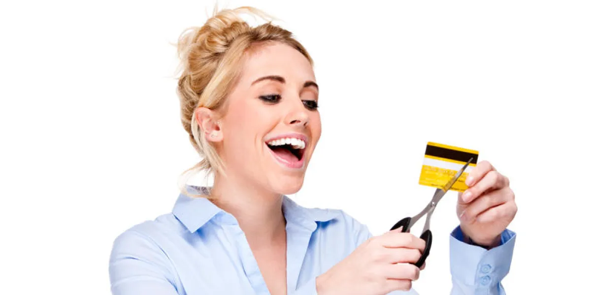 séduisante jeune femme regardant heureux découpant sa carte de crédit isolée contre blanc